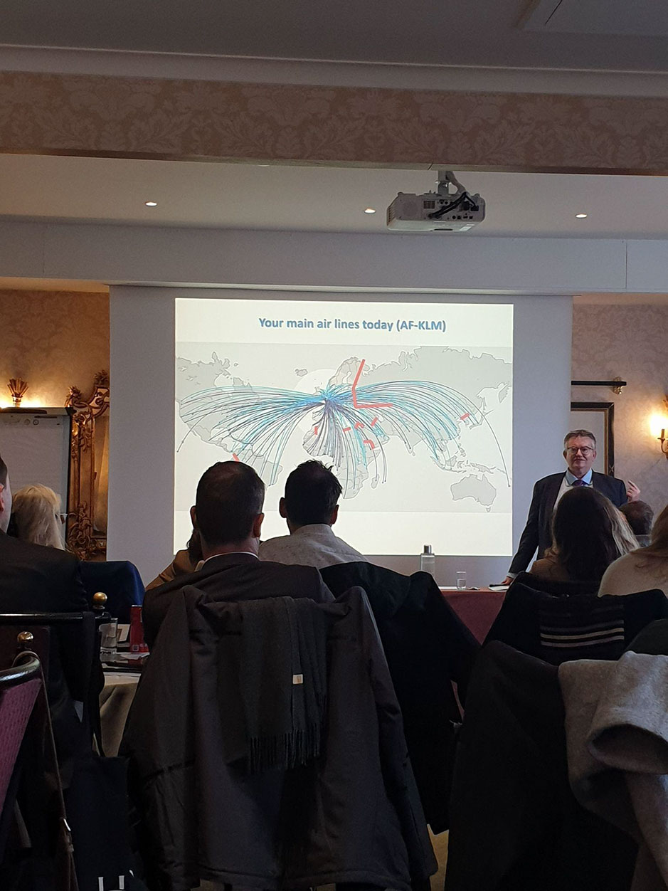 Group of people seated in a conference room, attentively listening to a speaker standing in front of a screen displaying a map illustrating the main airline routes of Air France-KLM