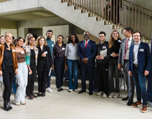 A group of people, including students and professionals, posing together at the 'Climate Day' event at HEC Paris. The image shows smiling participants, some holding certificates or documents, standing in front of a concrete staircase inside a modern building. On the right side of the image, a banner displays the logos of HEC Paris and Climate and Earth, with the text 'Climate Day'