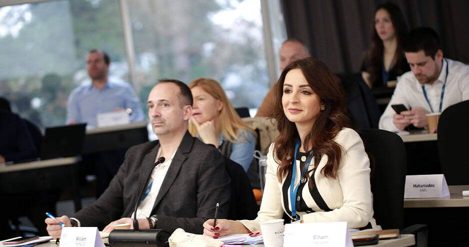 A group of people sitting at tables, likely in a classroom or conference room, engaged in a discussion or presentation.