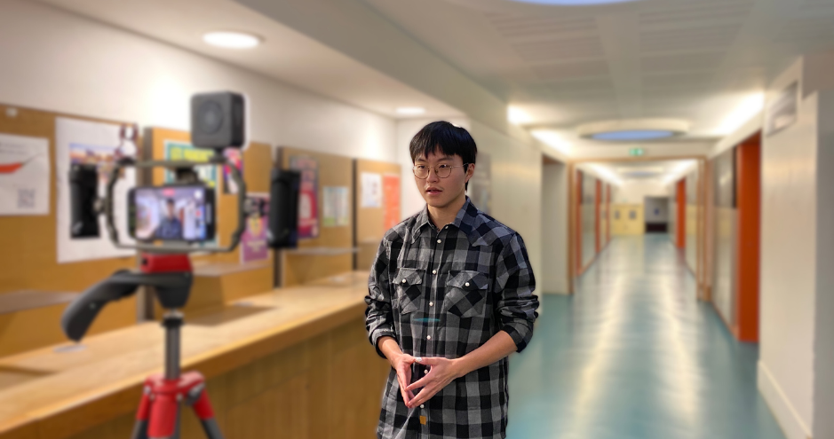 L'étudiant Santorin parle face à une caméra sur trépied dans un couloir éclairé.